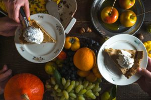 Pieces of apple pie with ice cream on plates, vegetables and fruits on Thanksgiving Day