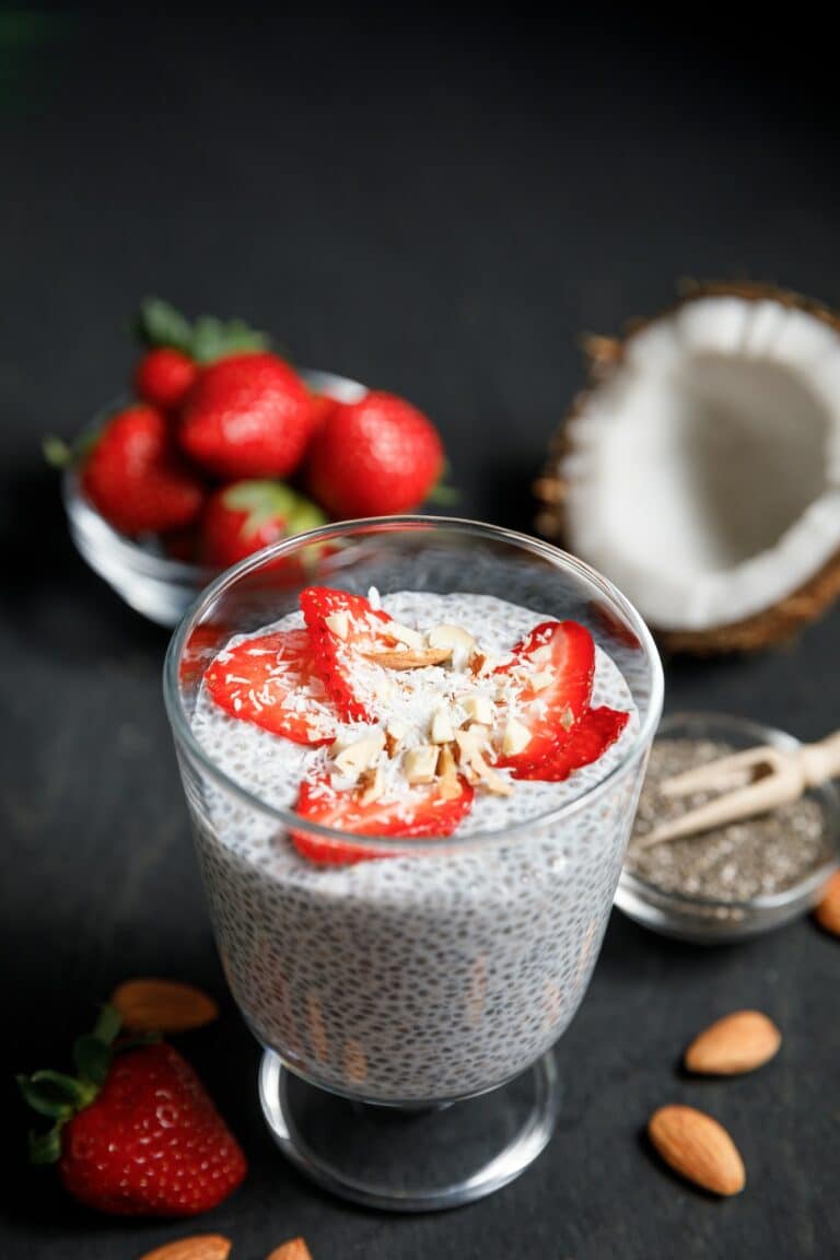 Chia seeds pudding with strawberries and coconut chips in glass on dark background.